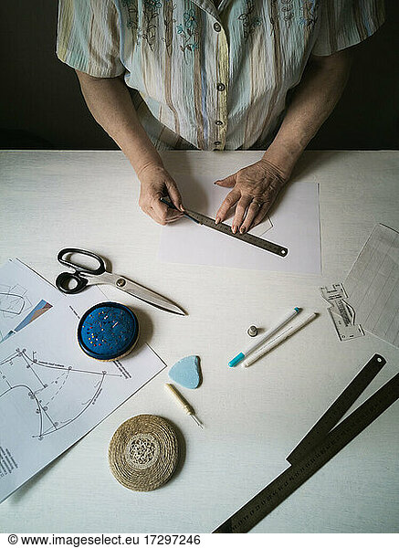 An elderly woman makes a pattern of a medical mask on a fabric