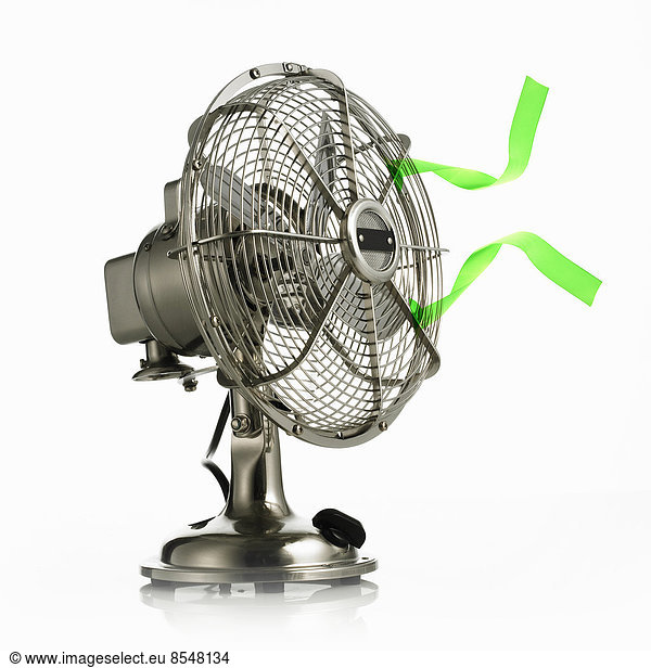 An electric fan with protective cage around the moving parts  and green streamers waving in the breeze.