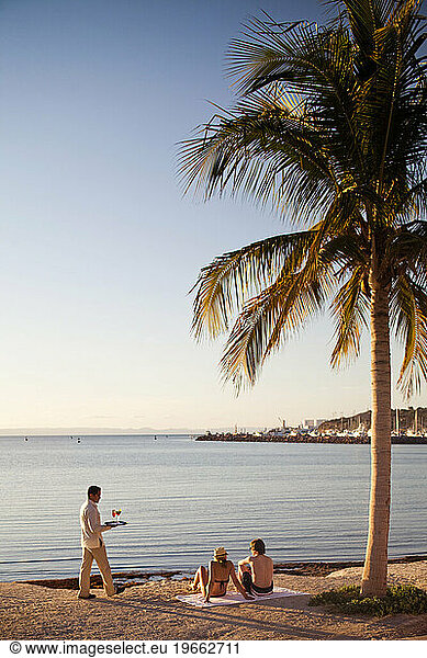 An employee carries drinks to a couple sitting underneath a palm tree next to the Sea of Cortes at a luxury hotel in La Paz  Mexico.