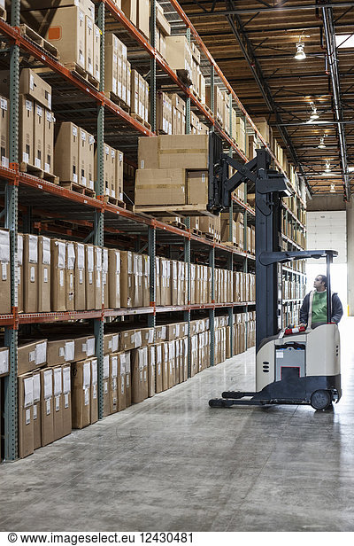 An employee picking products off a rack using a forklift stock picker in a distribution warehouse.