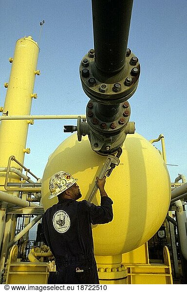 An oil drilling worker holds a large wrench and tightens a knob.