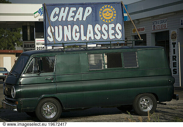 An old green van displays a sign for cheap sunglasses