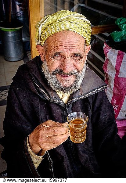 An old Moroccan man in traditional dress with a glass of mint tea outside his shop in the Medina in Marrakech  Morocco  North Africa.