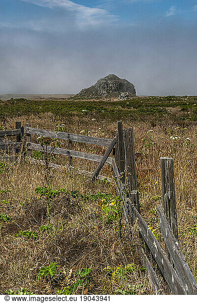 An old wooden fence in a field leading to a large rock in the fog