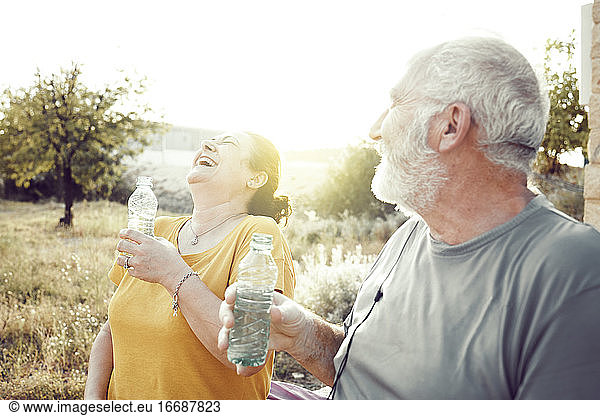 An older couple laughs while resting to drink water