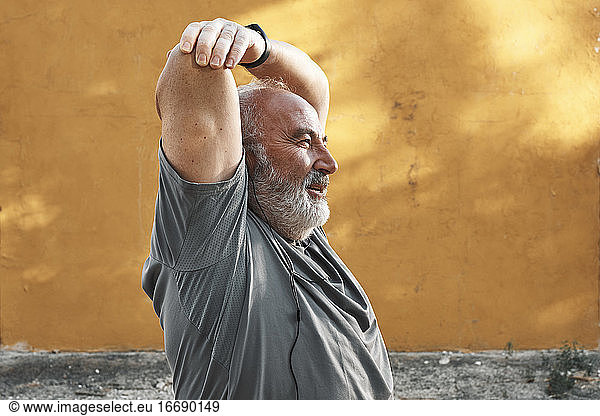 An older man with white hair and beard is stretching his arm