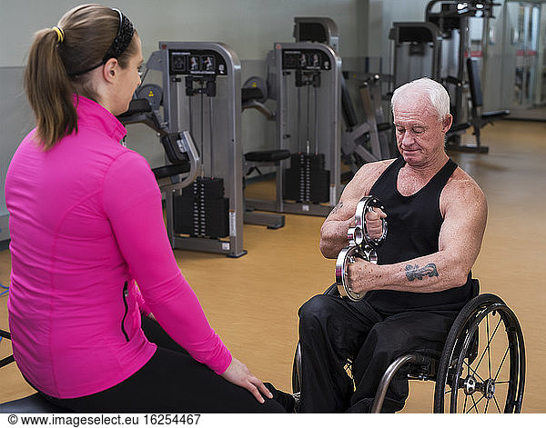 An older paraplegic man working out using a circular handheld device with the help of his trainer in fitness facility; Sherwood Park  Alberta  Canada