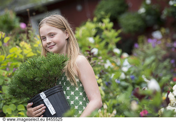 An organic flower plant nursery. A young girl carrying a plant in a pot.