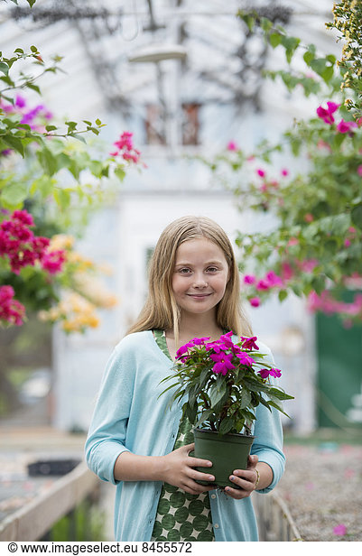 An organic flower plant nursery. A young girl holding a flowering plant.