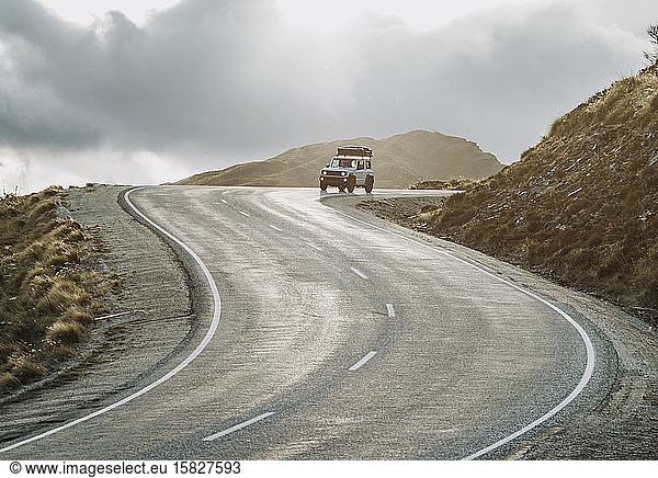 An SUV drives a twisting mountain road at sunset in New Zealand