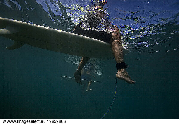 an underwater view of a senior surfer sitting on his surfboard