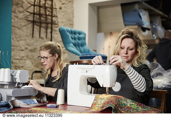 An upholstery workshop. Two women seated using sewing machines.