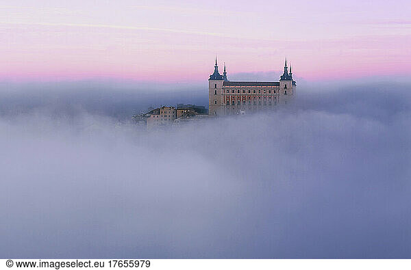 Ancient castle shrouded in mist in colorful purple sunrise