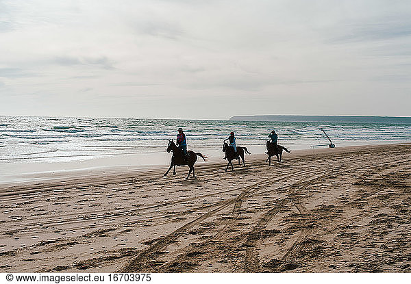 Andalusian horses running down beach in Spain with riders