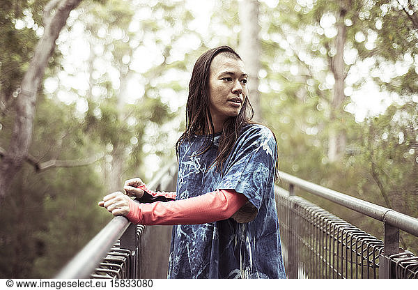 androgynous asian with ninja shave looks at forrest on tree top walk