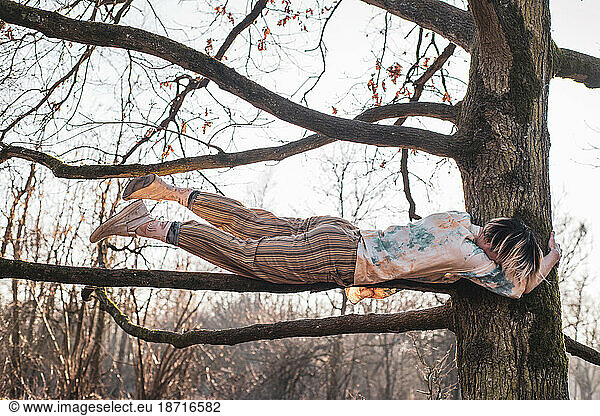 Androgynous dancer balances in strong hold along tree branch