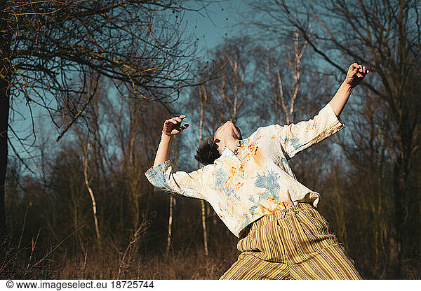 androgynous dancer dances freely with in nature with tree's and sun