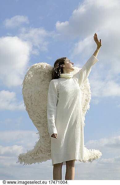 Angel wearing white wings with hand raised