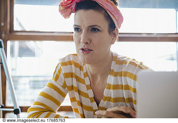 Angry woman wearing bandana sitting in front of window at home