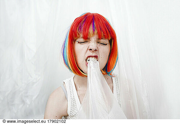 Angry woman with multi colored dyed hair biting plastic
