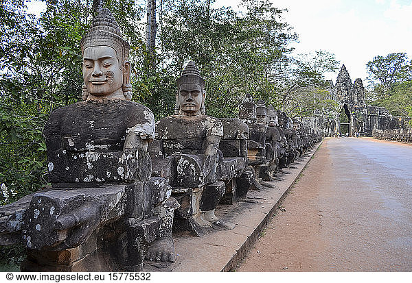 Ankor Wat  a 12th century historic Khmer temple and UNESCO world heritage site. Busts and statues of deities and guardian figures along a path to a stupa and entrance arch.