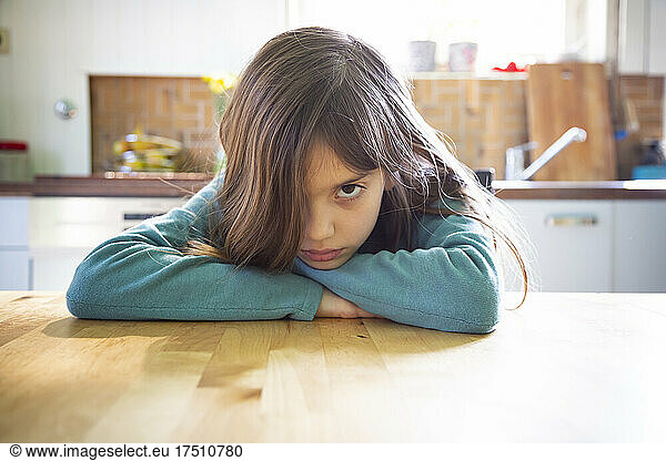Annoyed girl sitting in kitchen  leaning on table