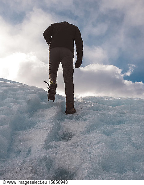 Anonymer männlicher Bergsteiger benutzt Spikes beim Klettern auf verschneiten Berg
