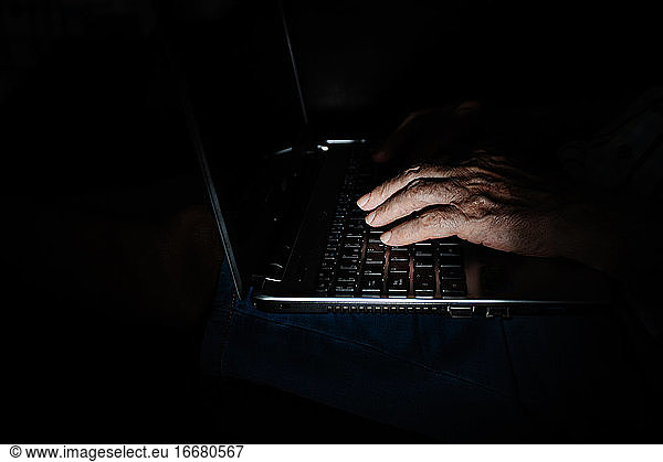 Anonymous aged person using laptop in darkness