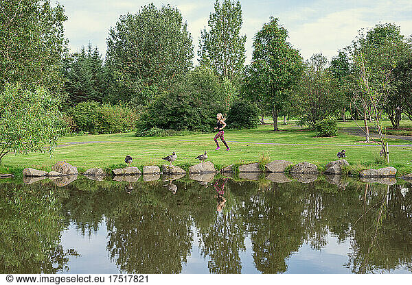 Anonymous lady jogging on grassy lake shore in park