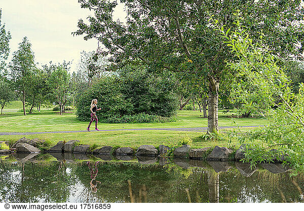 Anonymous sportswoman jogging near pond during training in park