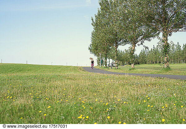 Anonymous sportswoman jogging on road near grassy field in rural area