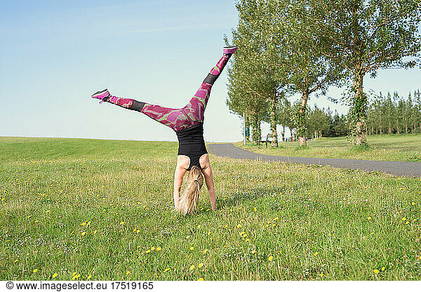 Anonymous sportswoman practicing handstand on grassy meadow