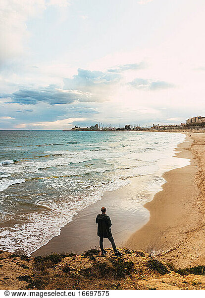 Ansichten eines Mannes von hinten mit Blick auf einen Strand in einem bewölkten Himmel