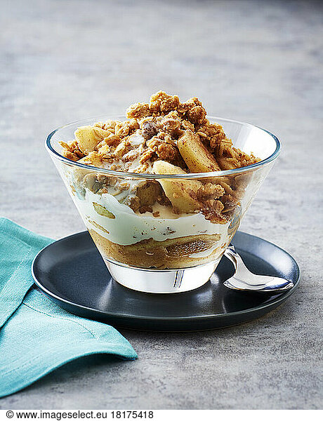 Apple crumble with cream in a glass bowl on a teal saucer