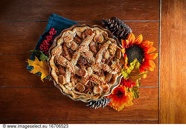 apple pie decorated with fall seasonal props on a kitchen table