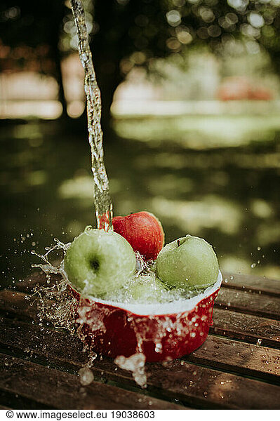 Apples in a bowl under running water.