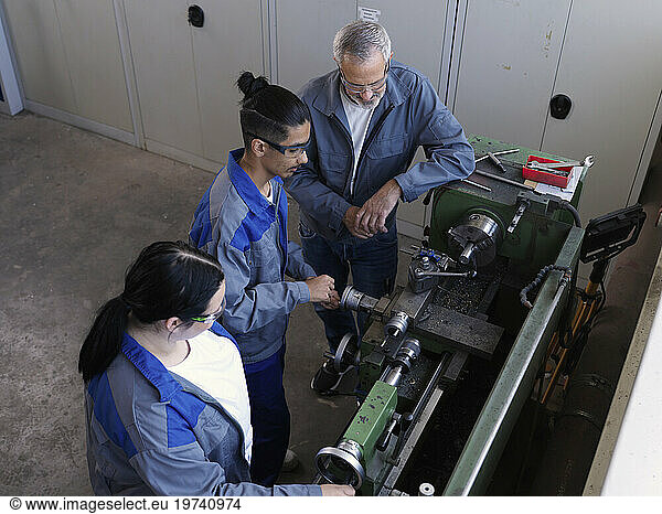 Apprentices learning lathe machine with instructor at workshop