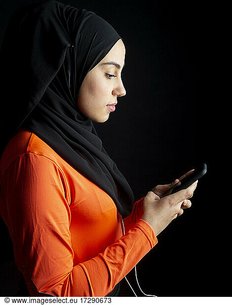 Arabische Frau mit Smartphone vor schwarzem Hintergrund