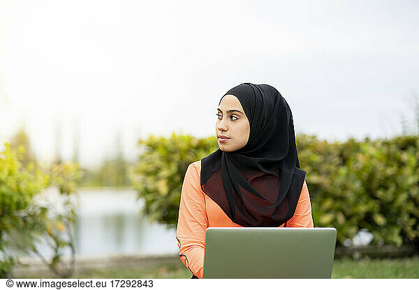 Arabische Frau schaut mit Laptop im Park weg