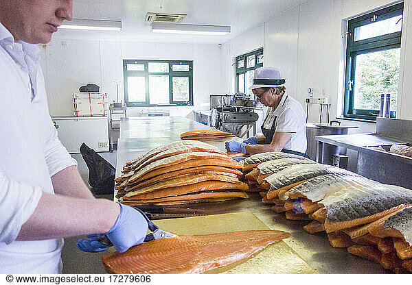 Arbeiter  der Fisch schneidet  während ein älterer Arbeiter an der Theke eines Lebensmittelverarbeitungsbetriebs arbeitet