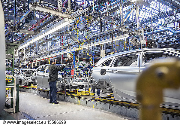 Arbeiter montiert in Autofabrik Motorhauben auf Autos