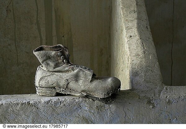 Arbeitsschuh aus Leder auf Mauer  verrottete Schuhe am Boden  verrotteter Schuh  Schuhwrack  vergammelter Treter  ausgelatschter Schuh  abgetragener Schuh