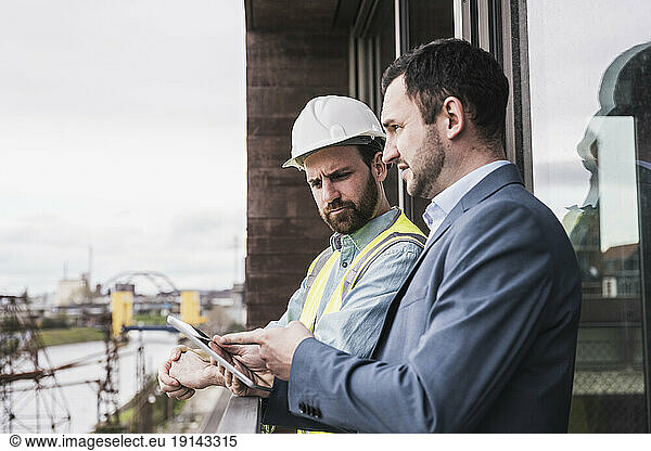 Architect explaining building contractor over tablet PC by railing