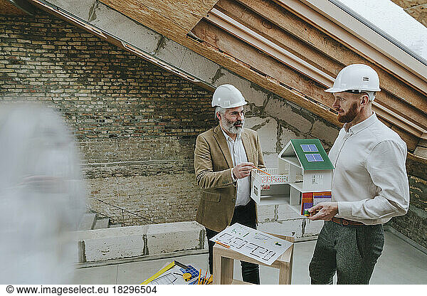Architect explaining colleague standing with house model at construction site
