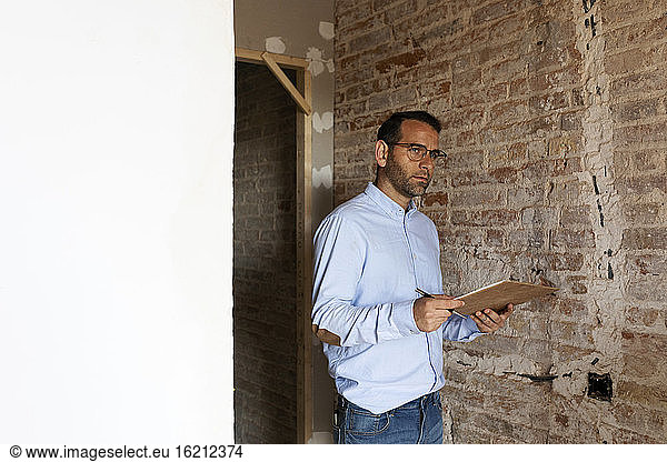 Architect holding clipboard at brick wall in a house under construction