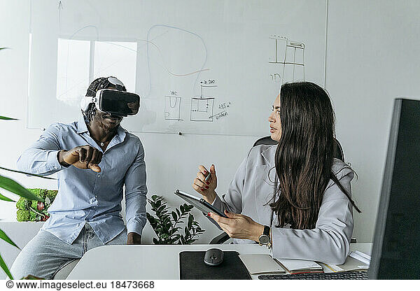 Architect holding tablet PC discussing with colleague wearing virtual reality headset at office