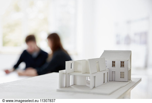 Architect's model of a building with two people at a meeting out of focus in the background. Communication.