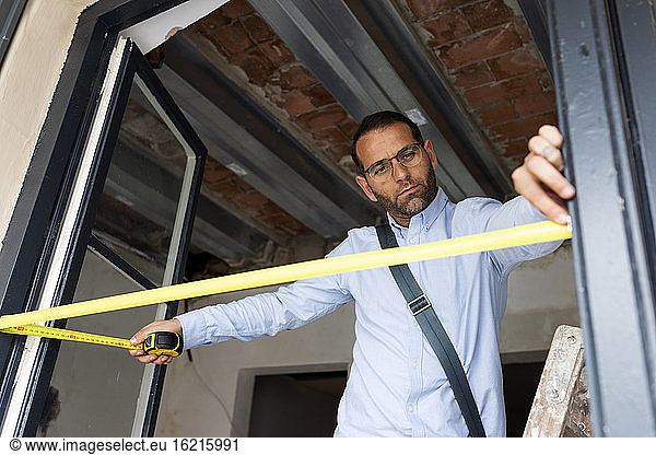 Architect using tape measure on window frame in a house under construction