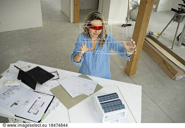 Architect wearing virtual reality simulator gesturing and examining house model