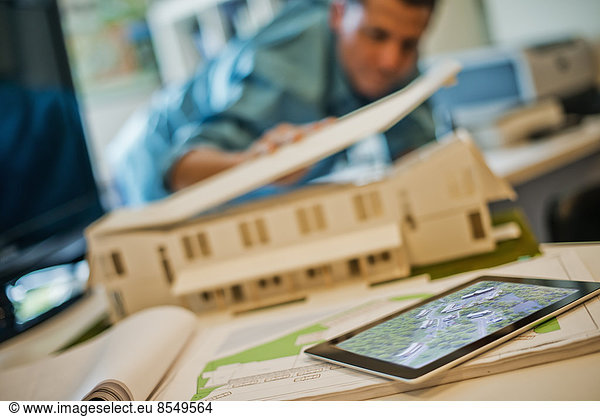 Architects working on a green construction project  using computer technology  in an office. An architect's model of a house. Computer tablet.